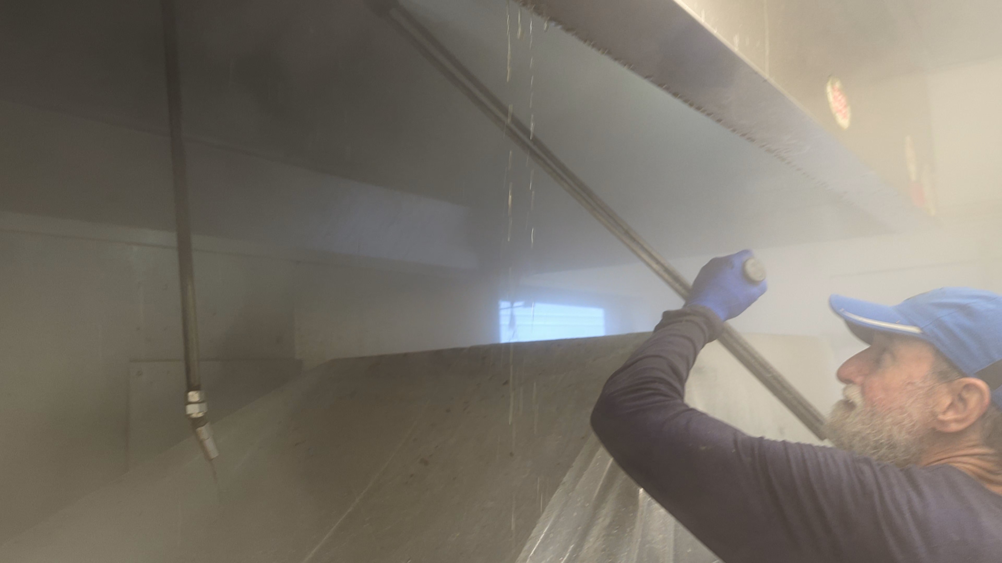 Technician cleaning a kitchen hood system with steam or pressure washer